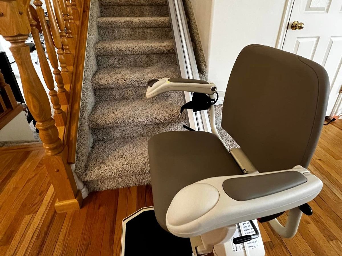 Lazo install: brown-seated lift at the foot of a carpeted staircase with an oak railing and wood floor