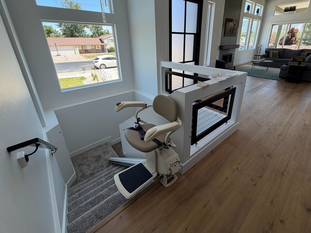 Tan stair lift parked open at the head of the stairs on a wood-floored landing