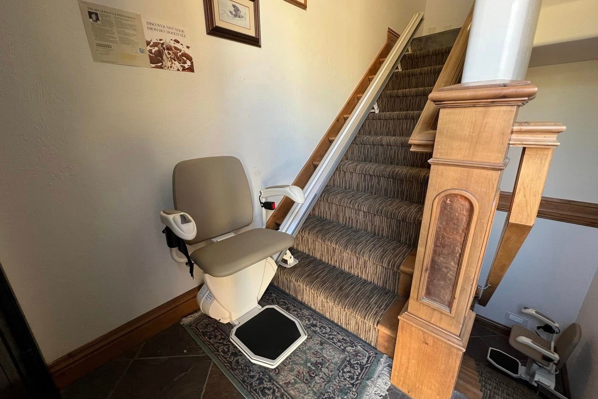 Harmar SL600 stair lift at the foot of a carpeted staircase beside a carved wood newel post